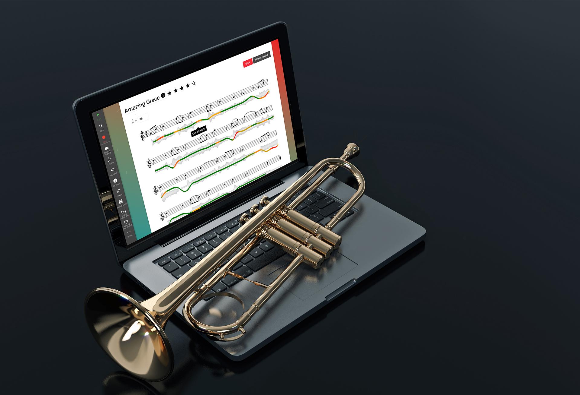 Laptop computer on dark grey background. A trumpet is laying across the keyboard and PracticeFirst software is displayed on the laptop screen.